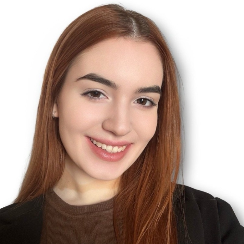Young woman with long straight red hair smiling, wearing a brown top and a black jacket, against a white background.