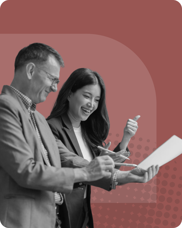 A man and woman in business attire smiling and discussing a document, with the woman giving a thumbs-up.