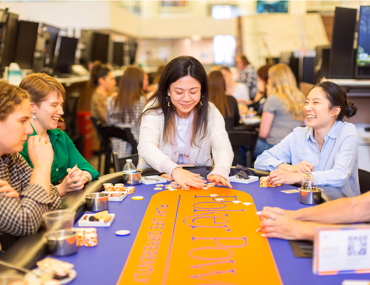 alt="A woman deals poker cards at a Poker Power event while others around the table laugh and engage."