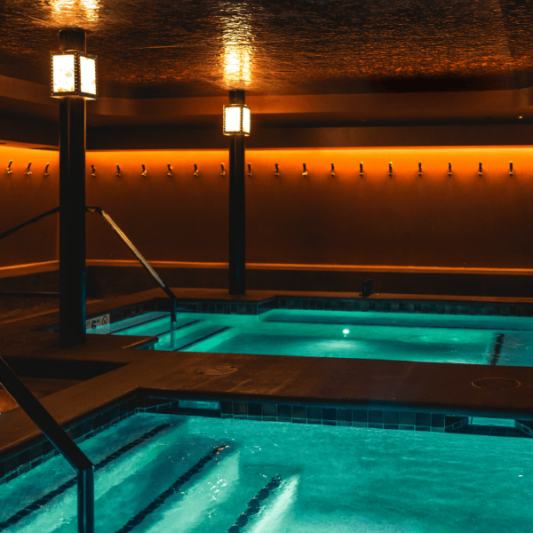 Modern bathhouse interior at Umvelt in downtown Bozeman, Montana, featuring a glowing warm spa and cold plunge pool with ambient lighting and minimalist design. Part of a full contrast therapy experience including a Finnish sauna, banya-style sauna, and steam room for deep relaxation, recovery, and social wellness.