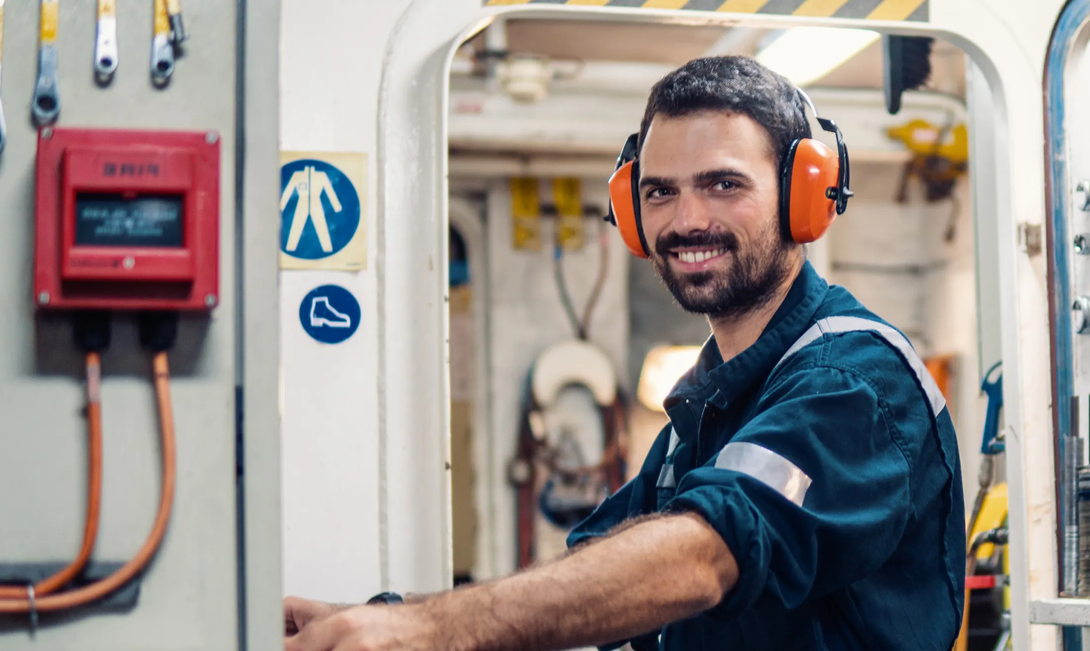 A QMED worker in a blue working outfit and safety gear smilling at the camera