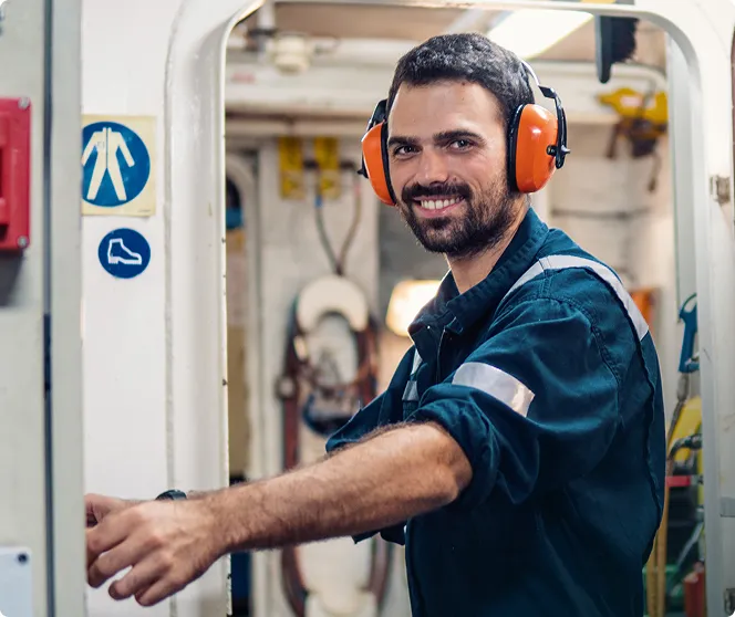 A QMED worker in a blue working outfit and safety gear smilling at the camera