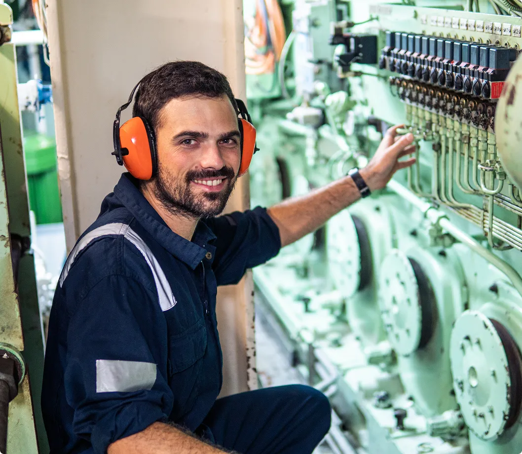 A QMED worker in a blue working outfit and safety gear smilling at the camera