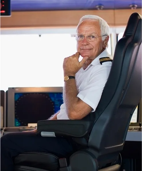 An old male sitting in a ship cabin looking at the camera