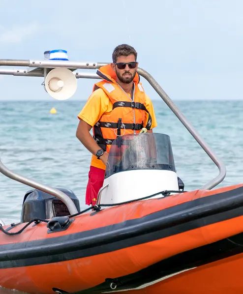 A male in a life jacket on a small boat driving it