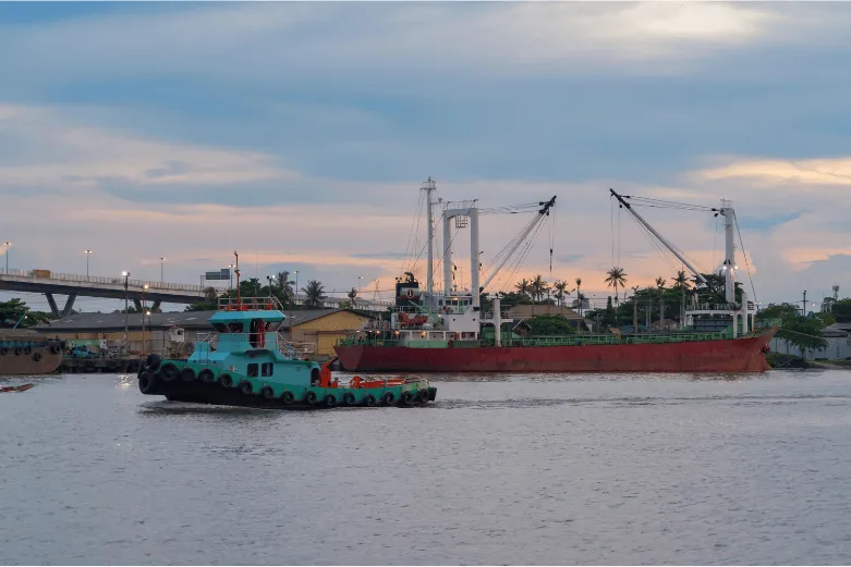 Blue tow boat in a harbor in front of a larger container ship