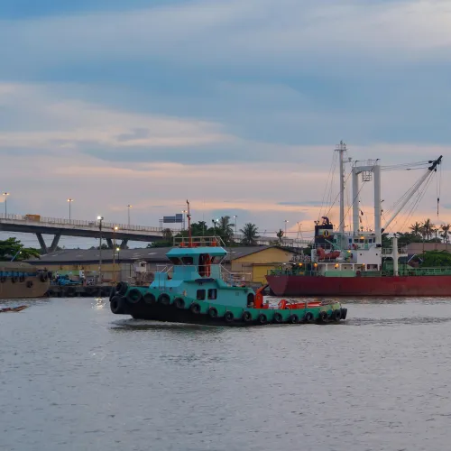 Blue tow boat in a harbor in front of a larger container ship