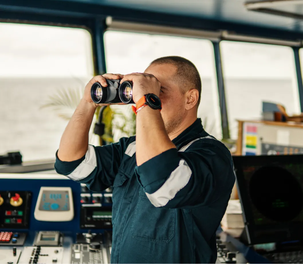 A captain in his cabin looking through binoculars