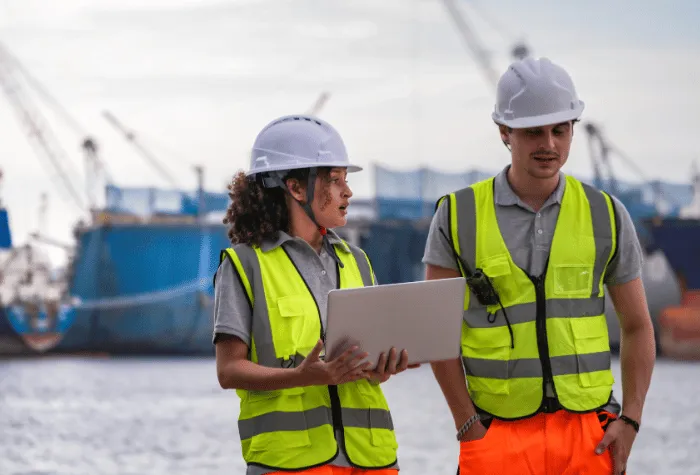 Two teammates in reflective vests discuss a project in a harbor