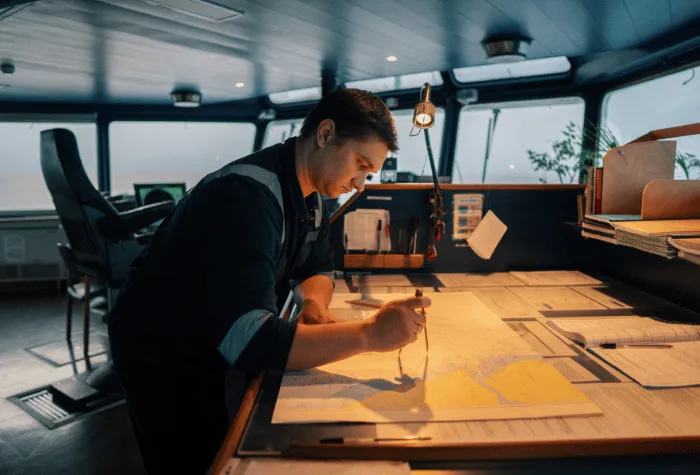 Mariner in bridge looking over nautical charts with plotting tools