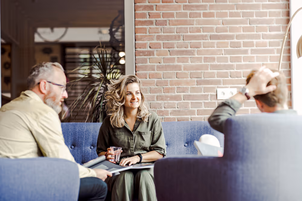 Een vrouw en twee mannen zitten in een ruimte met elkaar te praten