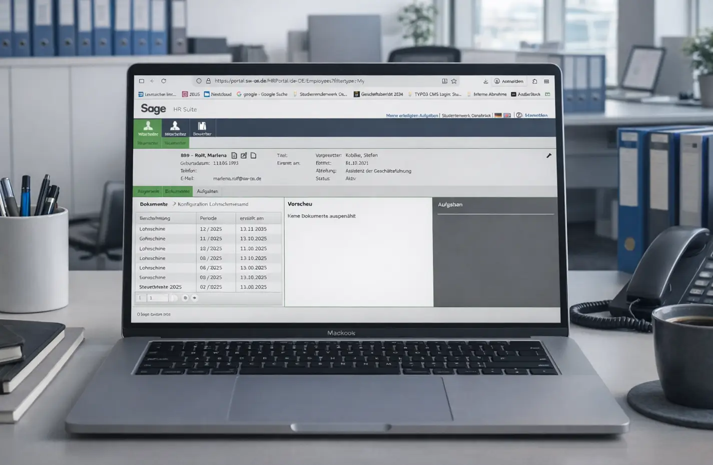 Laptop mit geöffneter Sage HR Suite Software zeigt Mitarbeiterdaten und Dokumentenübersicht auf einem Schreibtisch mit Stifthalter, Telefon und Kaffeetasse im Büro.