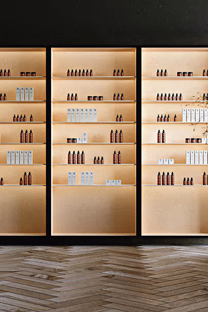 Étagères murales en bois clair rétroéclairées, alignées côte à côte, présentant des flacons bruns et des boîtes blanches de produits cosmétiques ou de soins, dans un intérieur au style minimaliste et élégant avec sol en parquet en chevrons.
