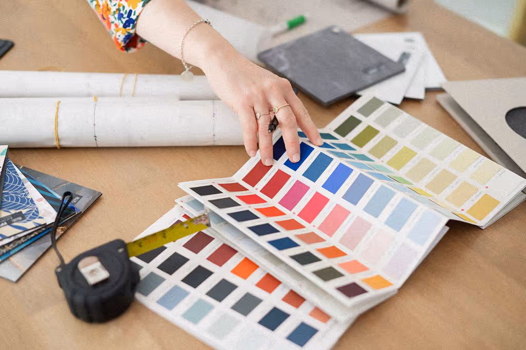 Une femme souriante tenant une palette de peinture et un mètre ruban, prête à commencer son travail créatif.