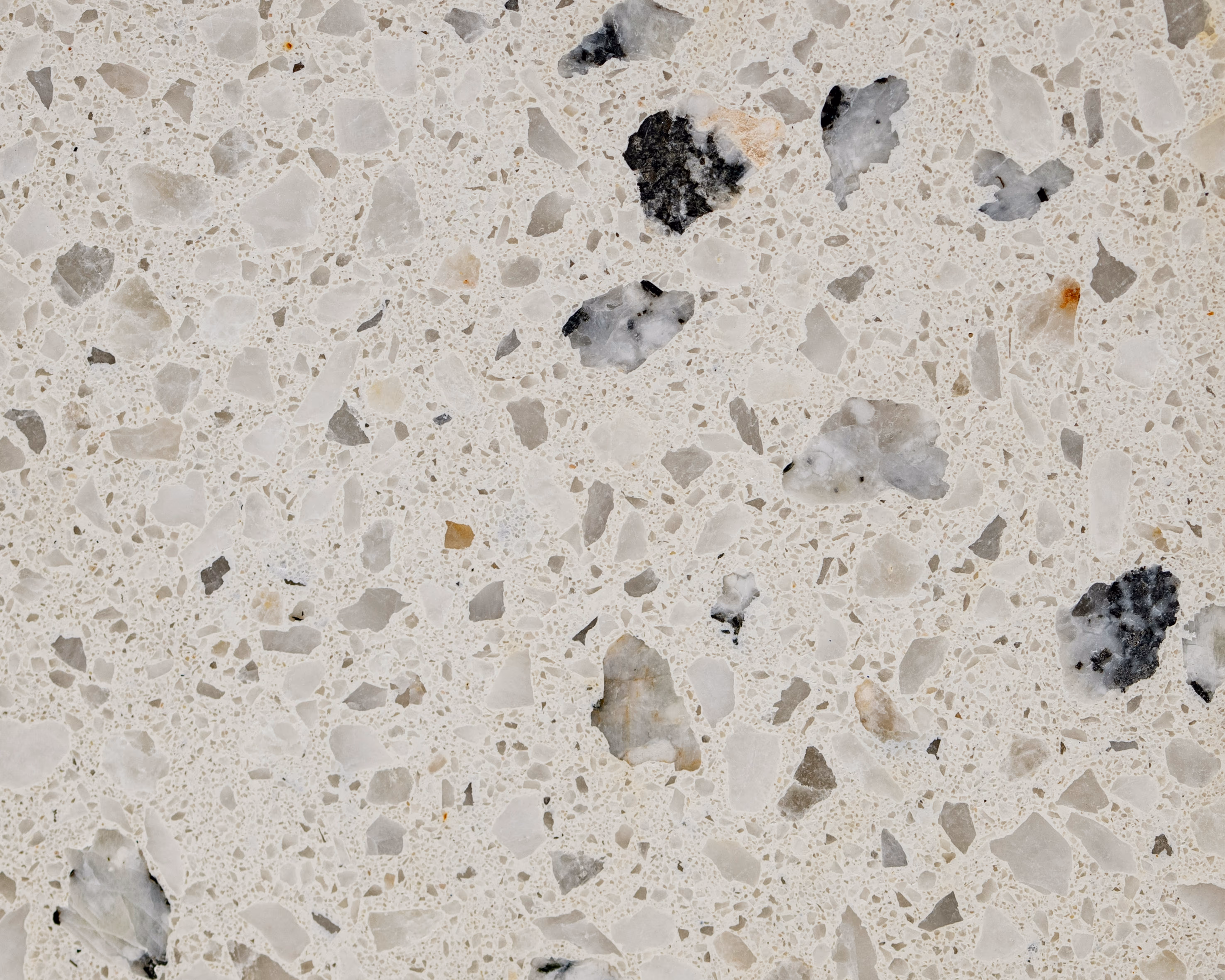 Surface de terrazzo beige clair avec des éclats de pierre irréguliers de couleurs variées, principalement gris, noirs et légèrement orangés.