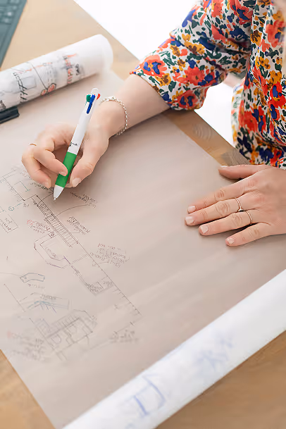 Une femme est en train de dessiner des plans d'architecture sur du papier avec un stylo.