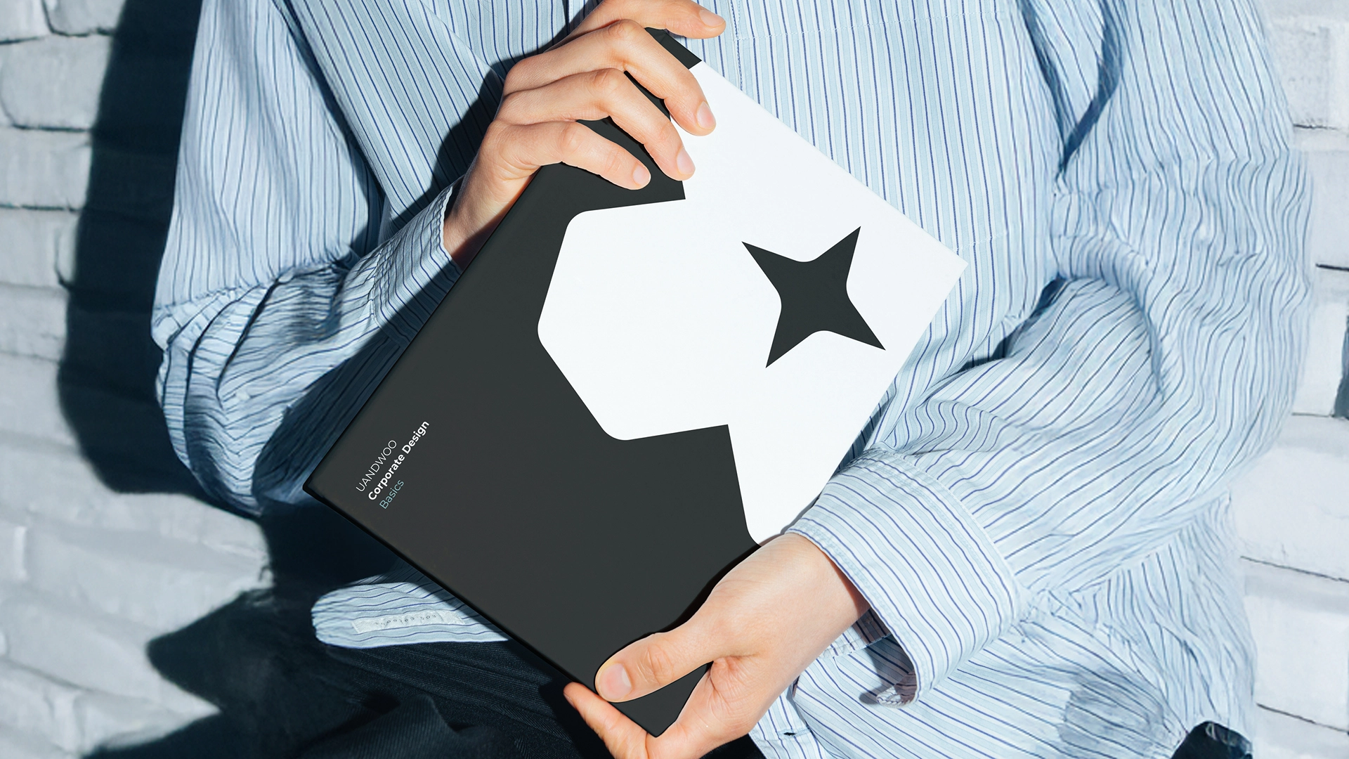 Das UANDWOO Corporate Design-Handbuch wird von einer Frau in der Hand gehalten