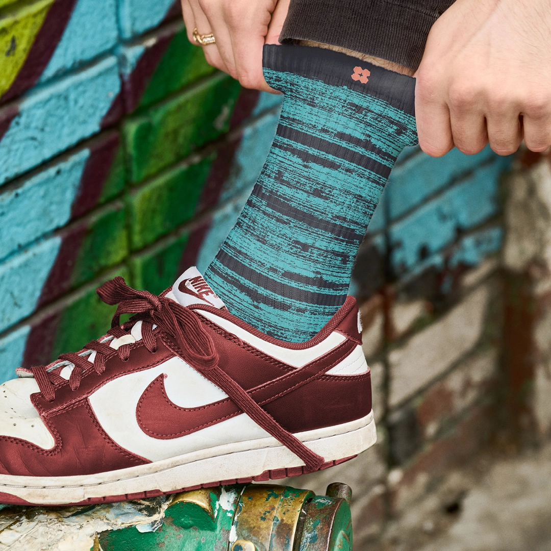 Ein Mann, der seine UANDWOO-Socke vor einer mit Graffiti besprühten Wand richtet