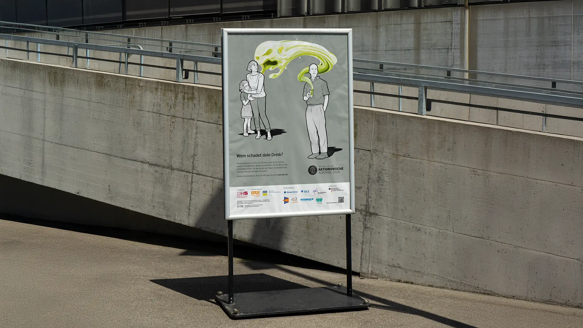 Plakat zur Sensibilisierung im Freien, auf dem ein Mann giftigen grünen Rauch in Richtung einer Frau und eines Kindes ausatmet, mit dem Text „Wem schadet dein Drink?“, wobei die sozialen Auswirkungen von Alkohol hervorgehoben werden