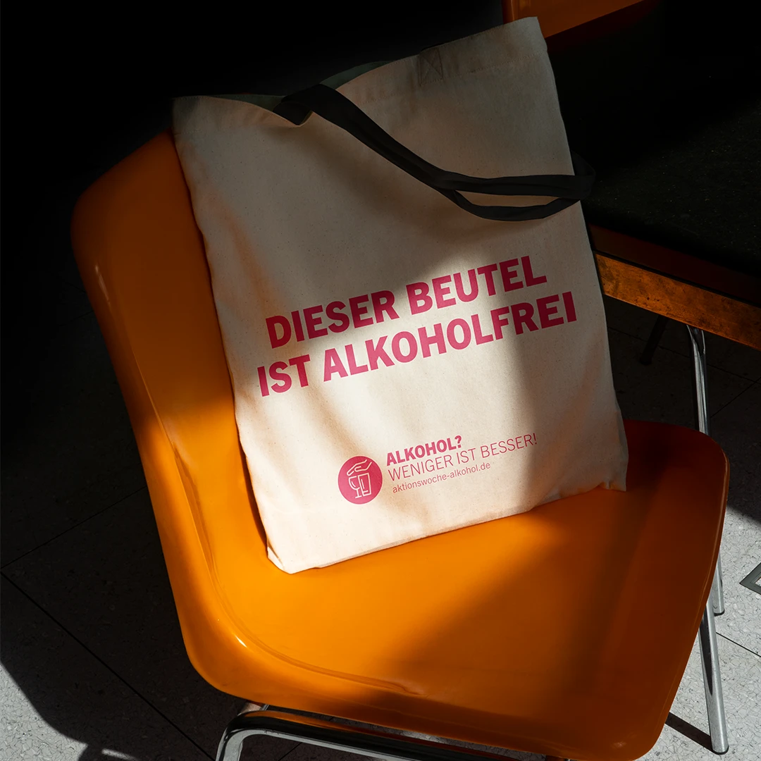 Stofftasche auf einem orangefarbenen Stuhl mit dem Slogan „Dieser Beutel ist alkoholfrei“, Teil der „Alkohol? Sensibilisierungskampagne „Weniger ist besser“