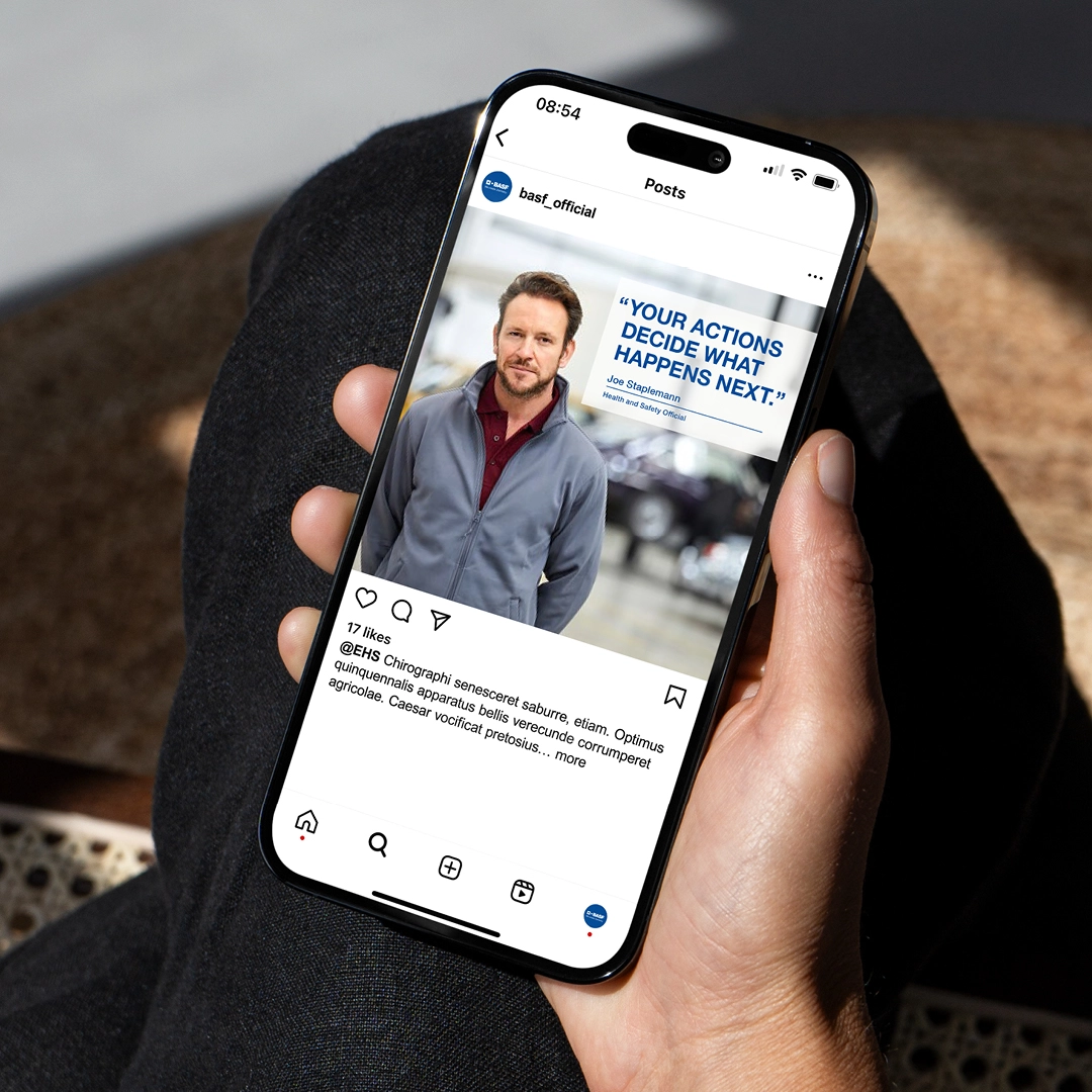Hand hält ein Smartphone mit einem BASF-Instagram-Post, der einen Mann in Arbeitskleidung und das Zitat „Your actions decide what happens next.“ zeigt