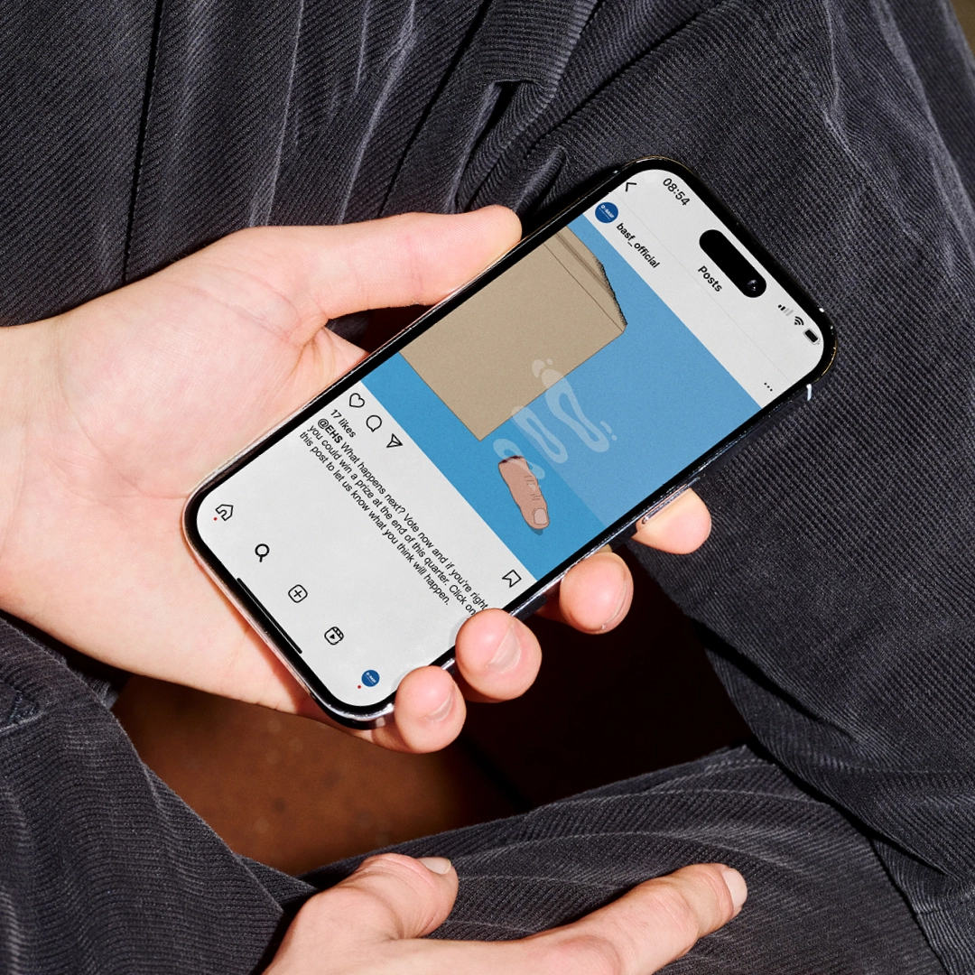 Person hält ein Smartphone mit einem BASF-Instagram-Post, der zeigt, wie ein abgeschnittener Finger neben einem Karton liegt