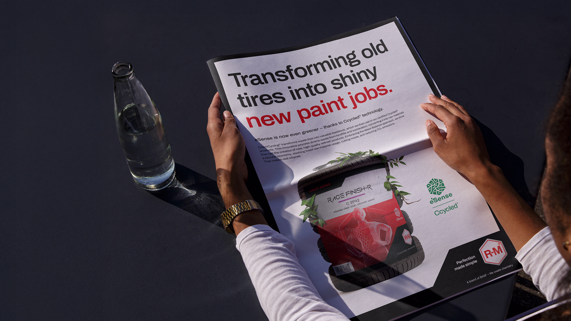 Person hält eine Zeitung mit Überschrift 'Transforming old tires into shiny new paint jobs' und Bild eines roten R-M eSense Lackierprodukts.