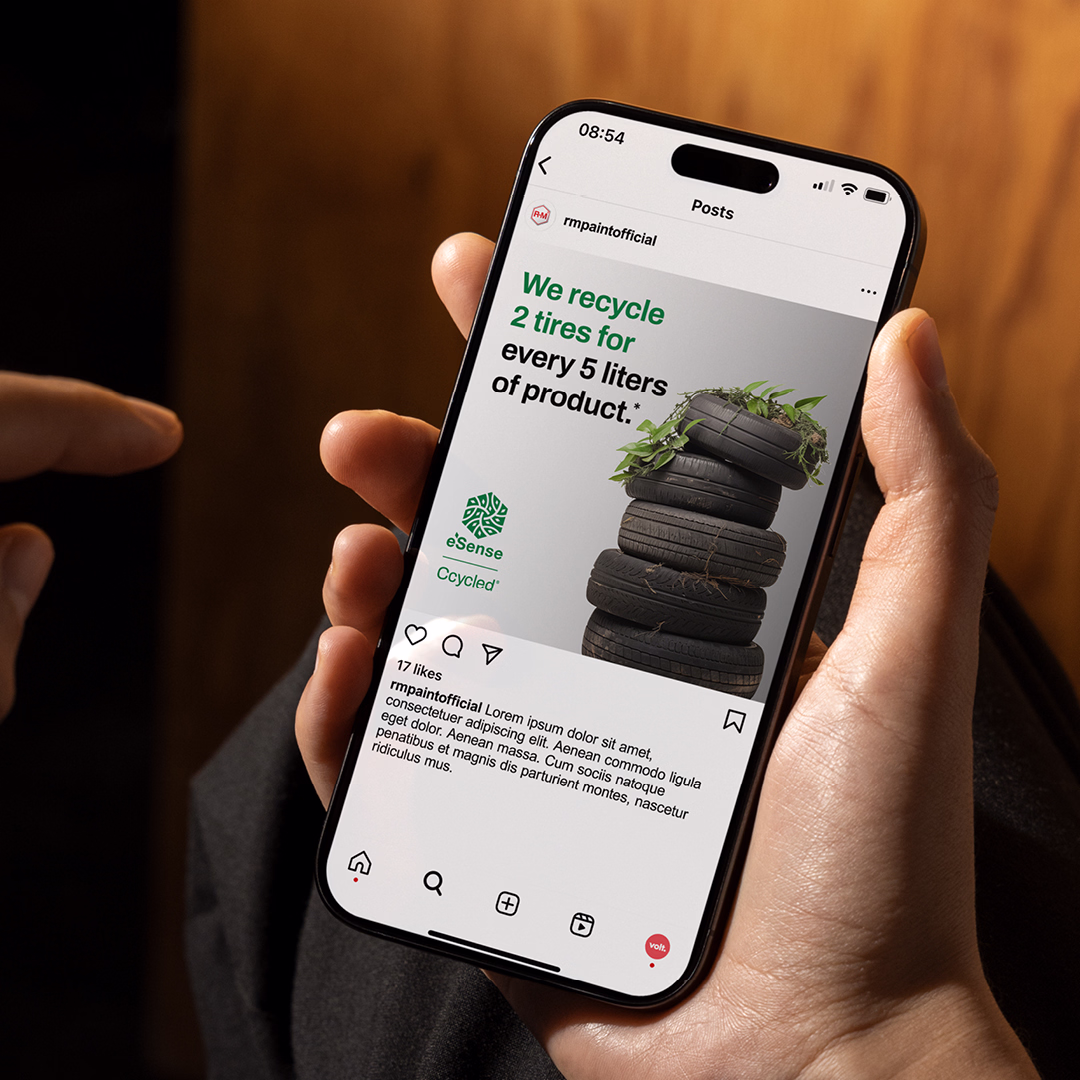 Hand hält Smartphone mit Instagram-Post von 'rmpaintofficial' über Recycling von 2 Reifen für alle 5 Liter Produkt, Stapel von 4 Reifen mit Pflanze oben.