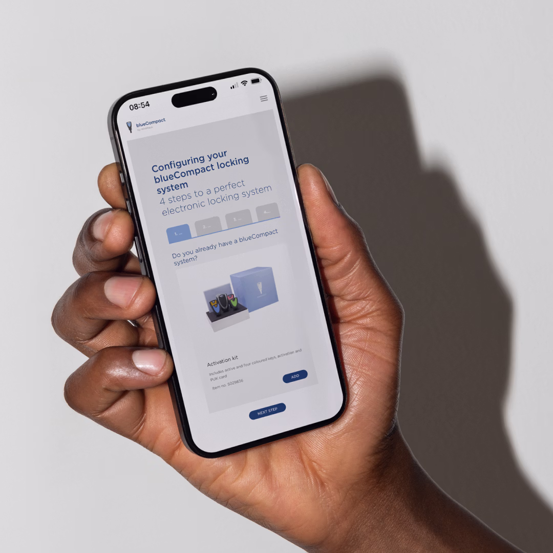 Hand hält ein Smartphone, das die Winkhaus Webseite mit der Überschrift 'The locking system with the app' und App Store-Buttons zeigt.