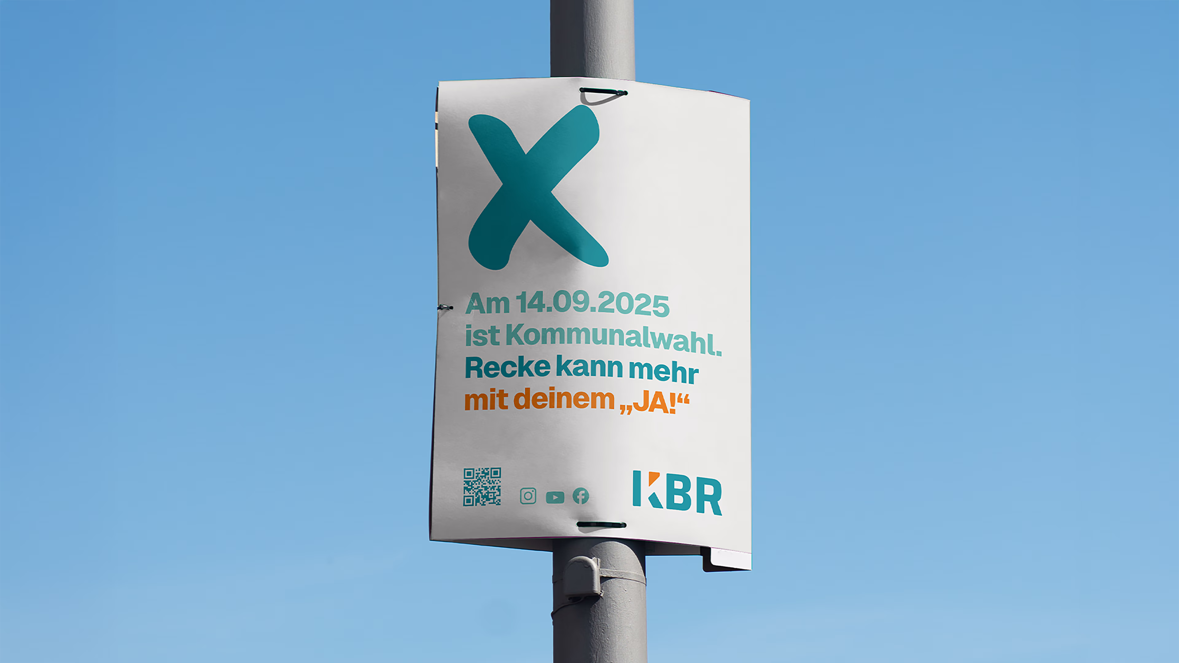 Ein KBR-Laternenmastplakat für die Kommunalwahlen 2025 mit dem Wahlkampfslogan „Recke kann mehr mit deinem ‚Ja!“ , ein QR-Code und das KBR-Logo vor blauem Himmel.
