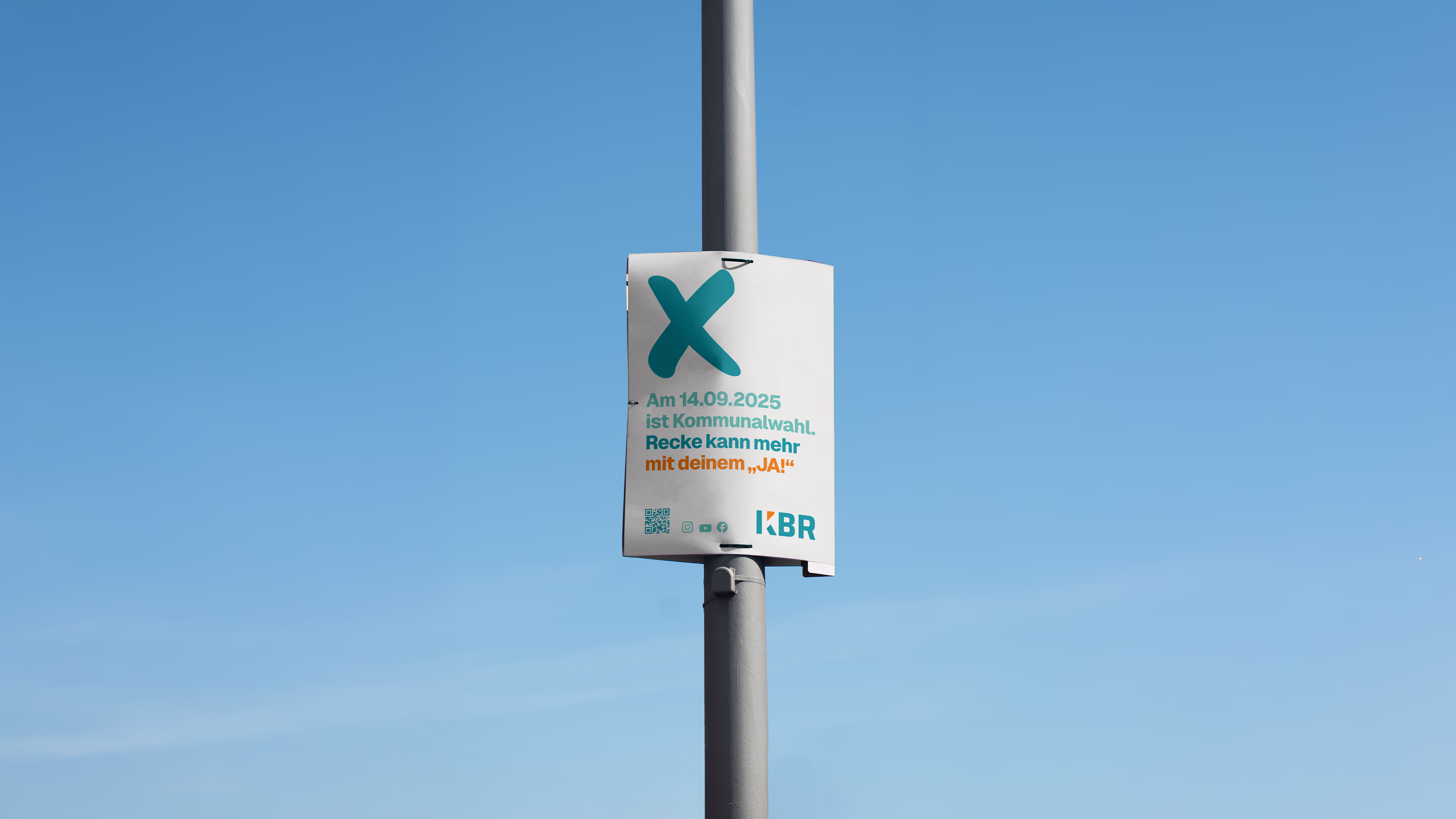 A KBR lamp post poster for the 2025 local elections featuring the campaign slogan “Recke can do more with your ‘Yes!’”, a QR code, and the KBR logo against a blue sky.