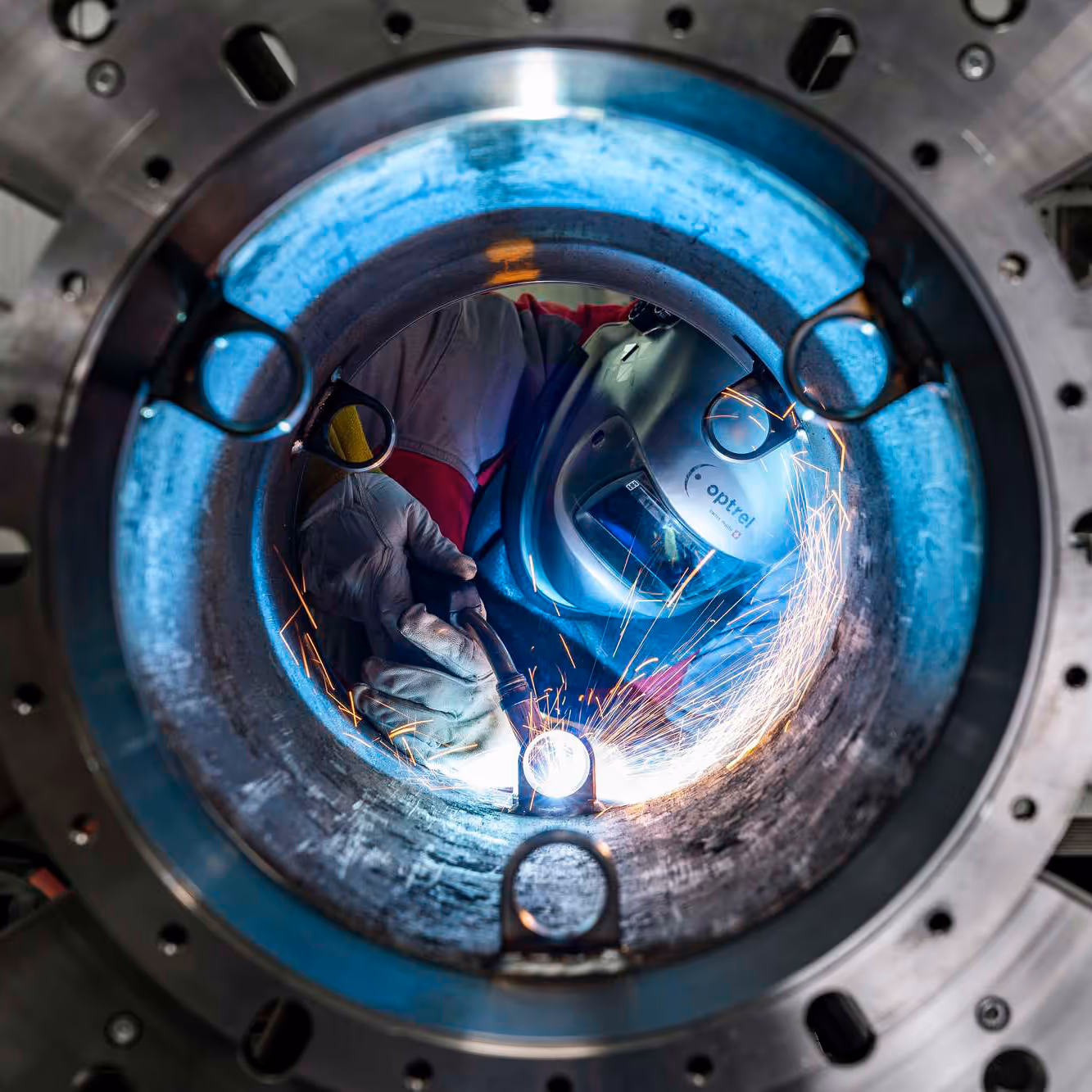 Schweißer mit Schutzhandschuhen und Helm schweißt in einem großen Metallrohr, bei dem Funken fliegen.
