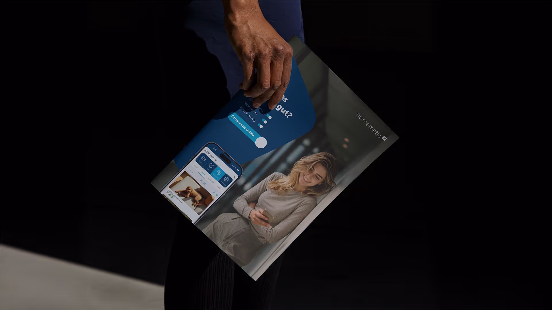 Person holding a magazine showing a smiling woman using a smartphone and a mobile app interface with a dog photo, under the brand name Homematic IP.