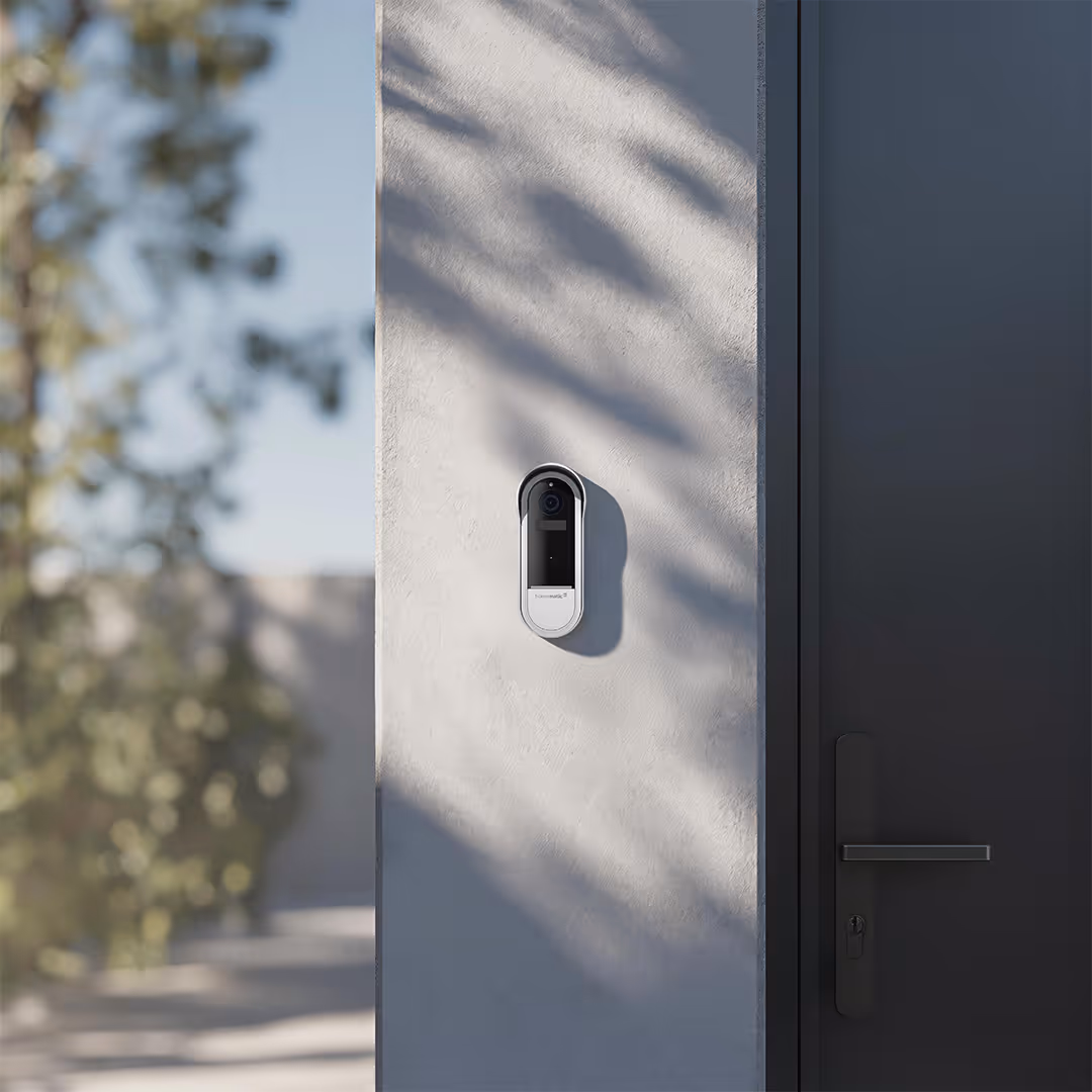 Smart video doorbell mounted on a light-colored wall next to a dark door handle.