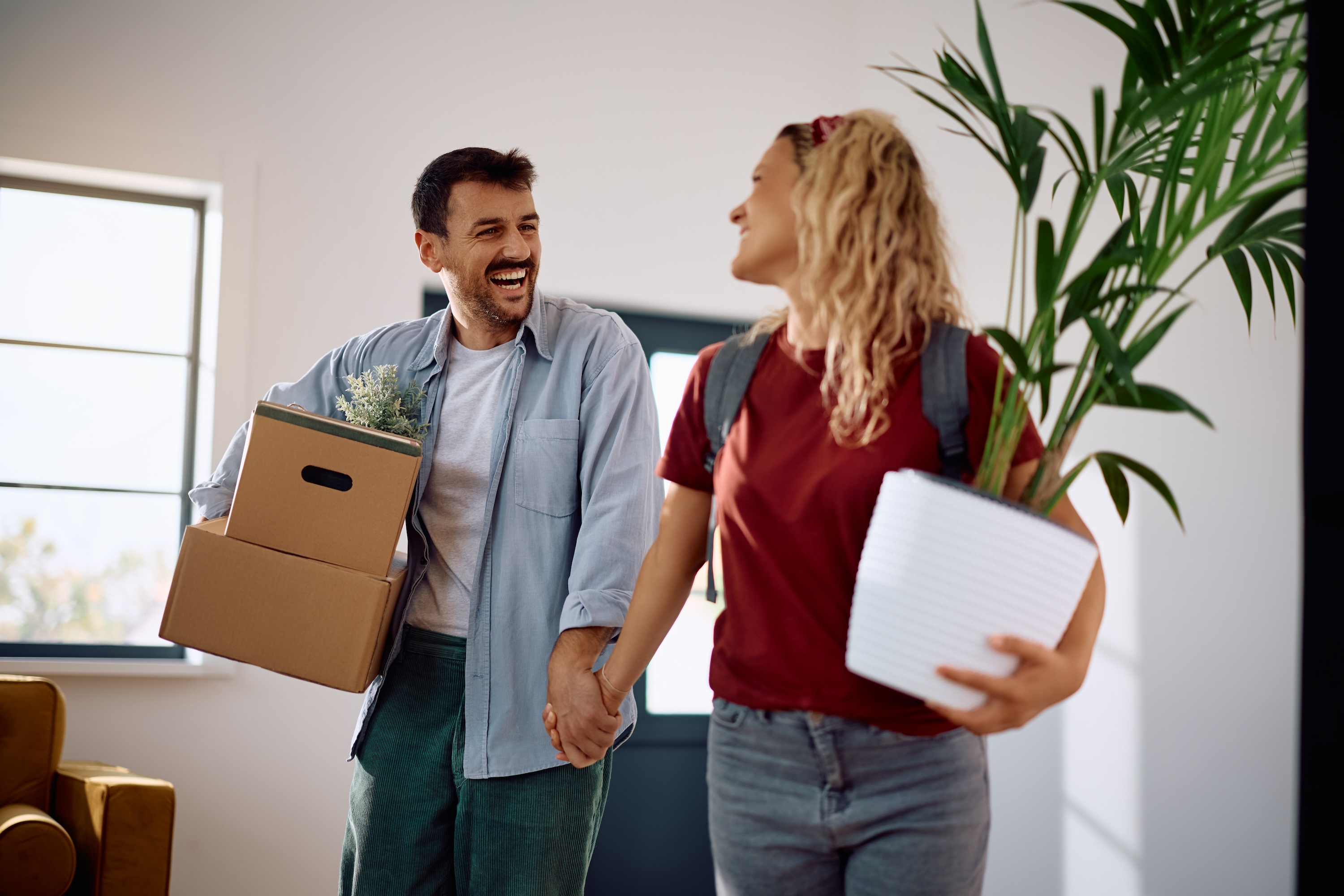 Happy residents carrying moving boxes and plants into a bright, open-concept home at The Cottages at Capital Circle in Tallahassee, FL, highlighting a seamless move-in experience