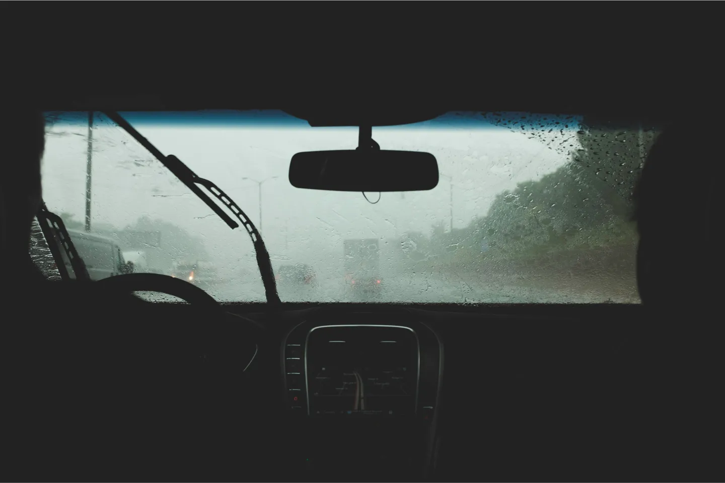View from inside a car during heavy rain, wipers moving, road and cars blurred by water.