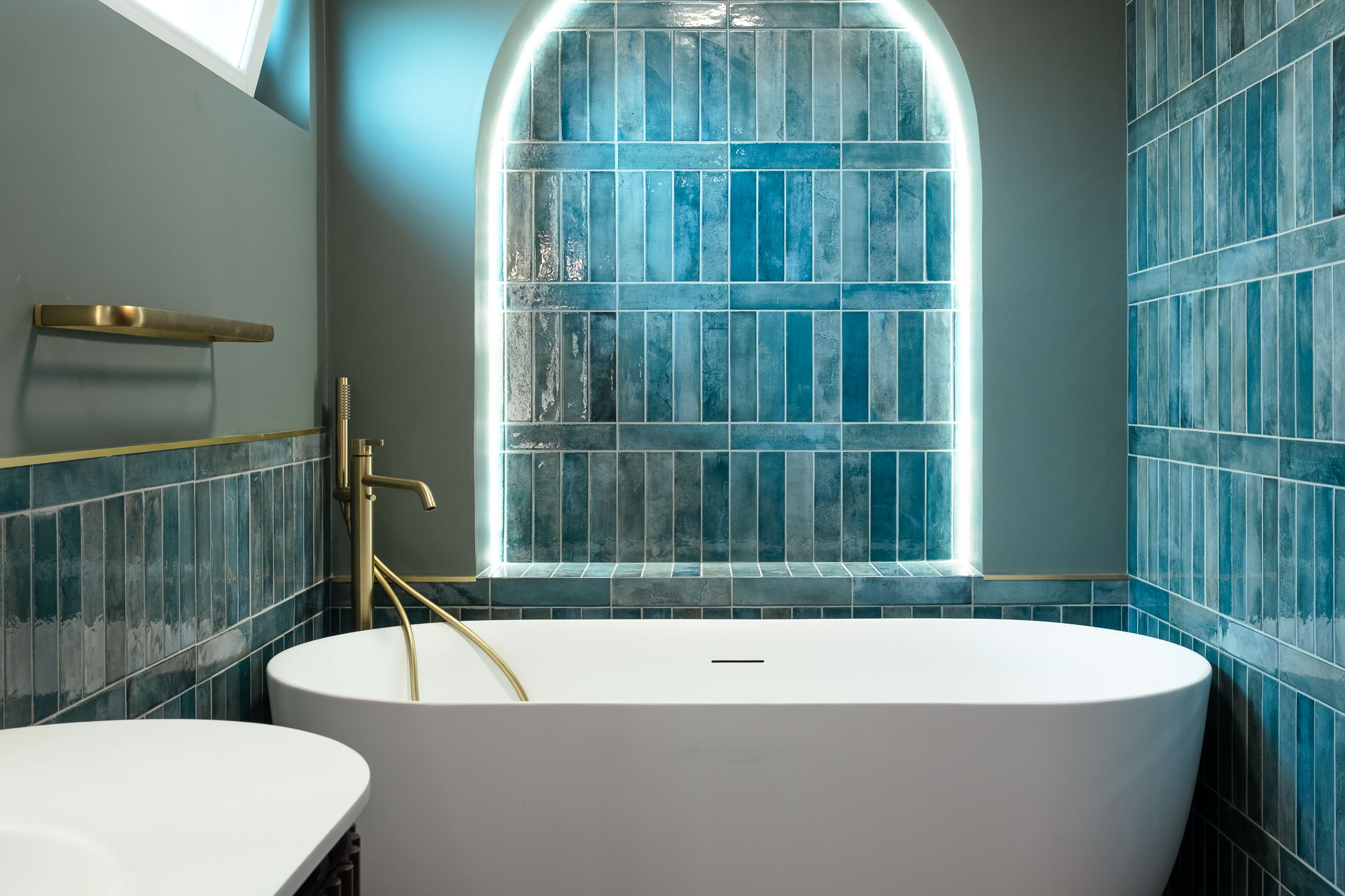 Salle de bain d'une maison à Mons-en-Barœul : baignoire îlot blanche, carrelage zellige bleu, niche cintrée rétroéclairée et robinetterie laiton.