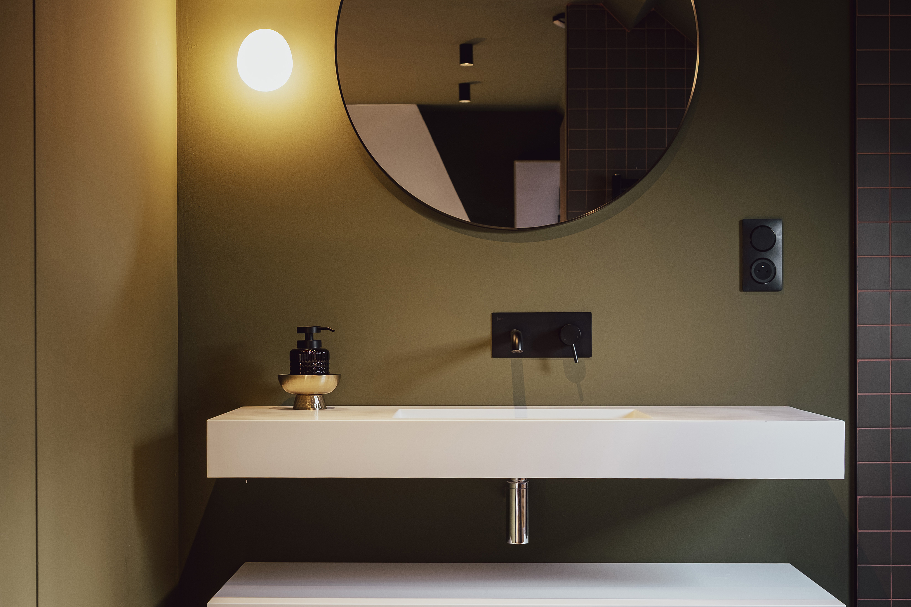 Salle de bain d'une chambre d'hôtes à Calais (Villa Verde) : murs vert olive, vasque suspendue blanche, robinetterie noire et miroir rond.