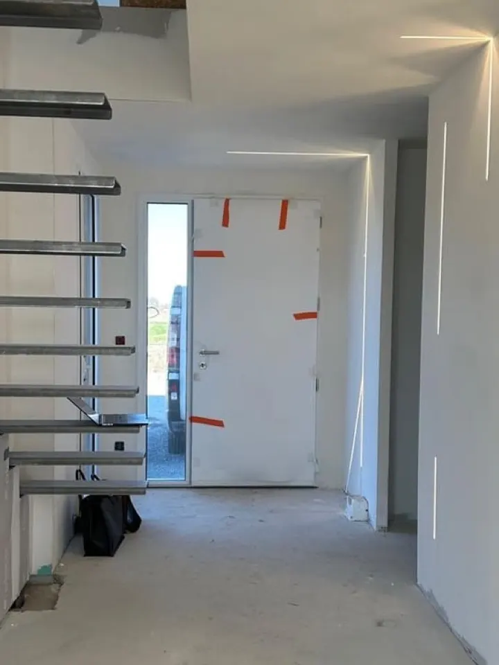 L'entrée de la maison pendant les travaux : escalier brut, murs en plaques de plâtre, sol en chape.
