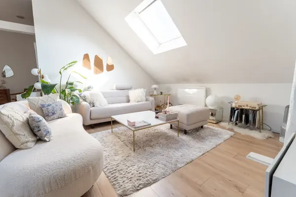 Salon lumineux d'un loft mansardé à Roubaix : canapé arrondi en bouclé blanc, table basse en marbre et laiton, grand tapis moelleux et velux.