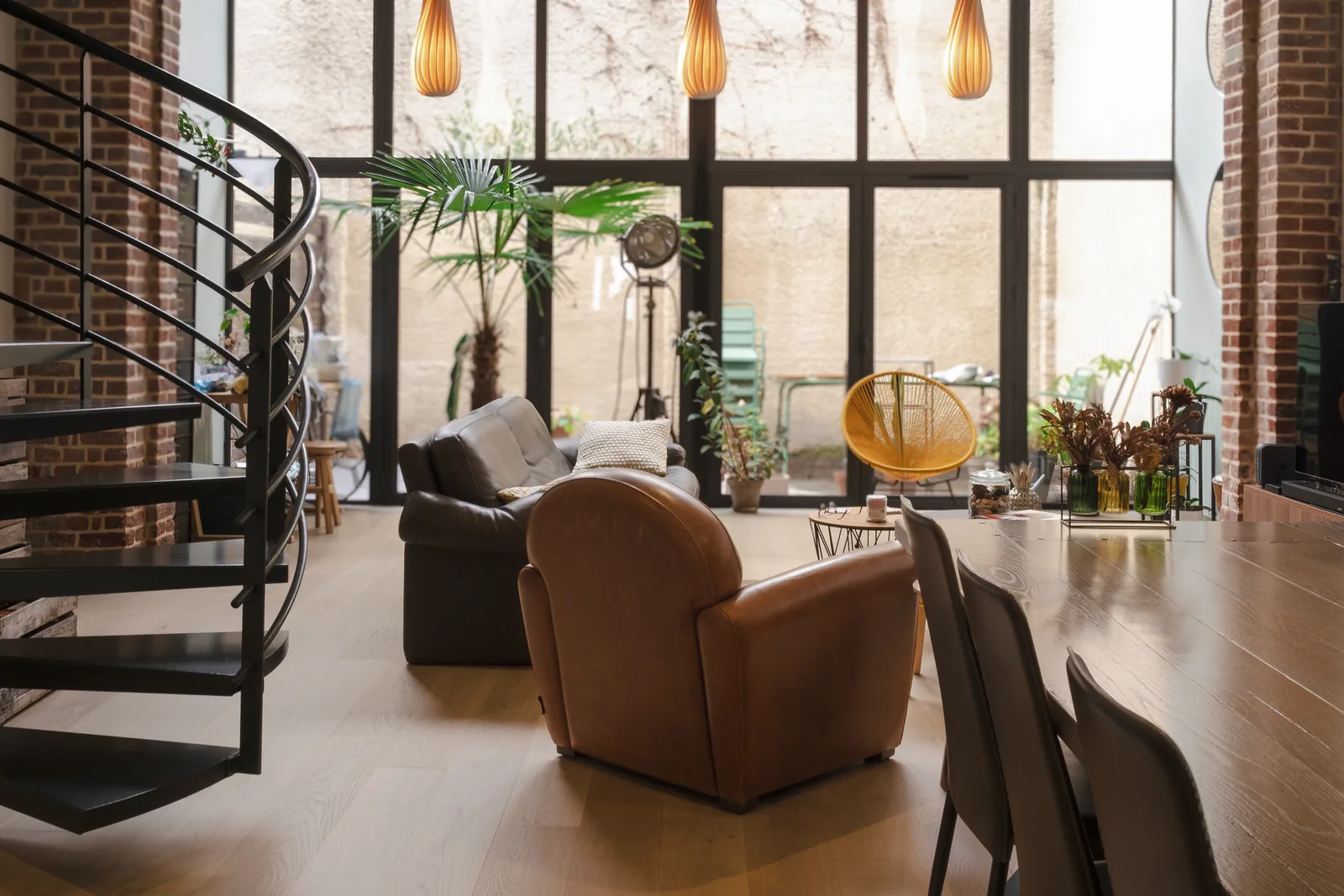 Loft avec escalier hélicoïdal noir, grandes verrières et fauteuils bruns.