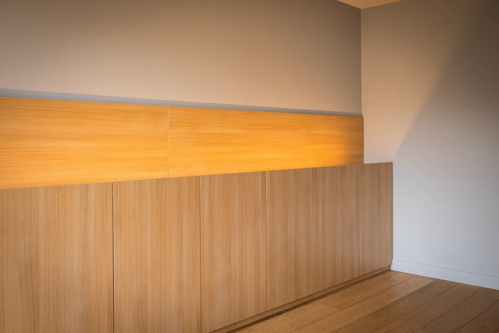 Meuble bas en chêne clair, panneaux verticaux et bandeau lumineux.