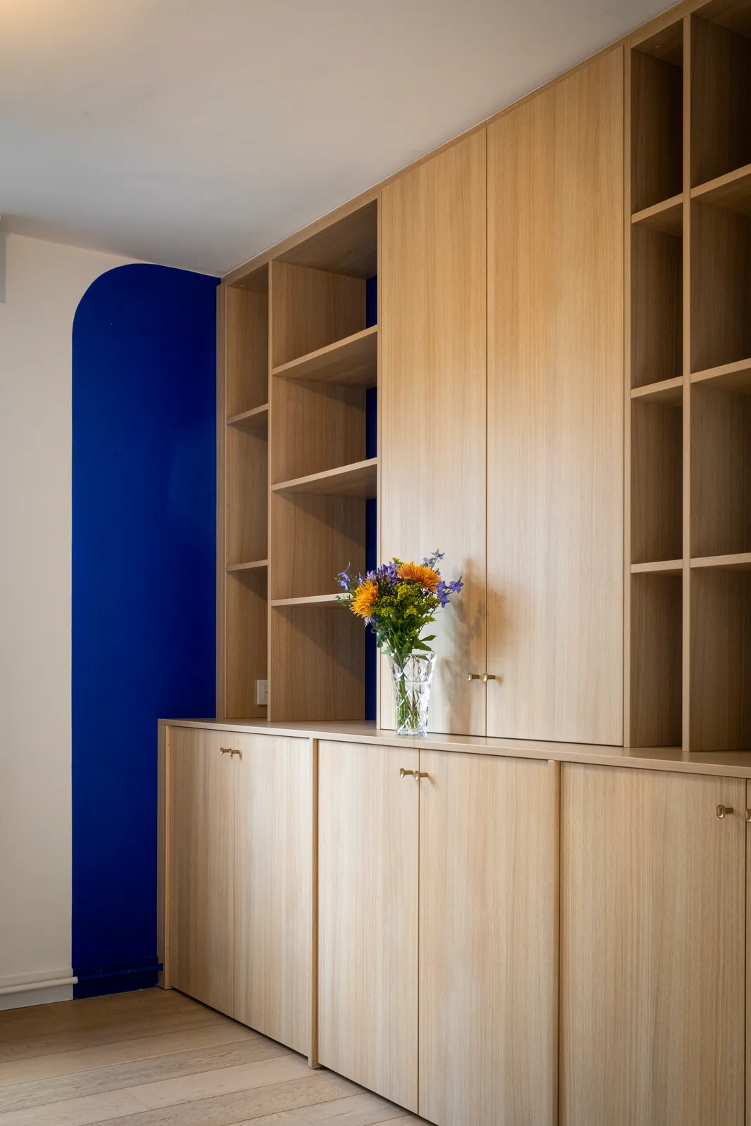 Rangements en chêne clair avec étagères ouvertes, niches bleues et fleurs.