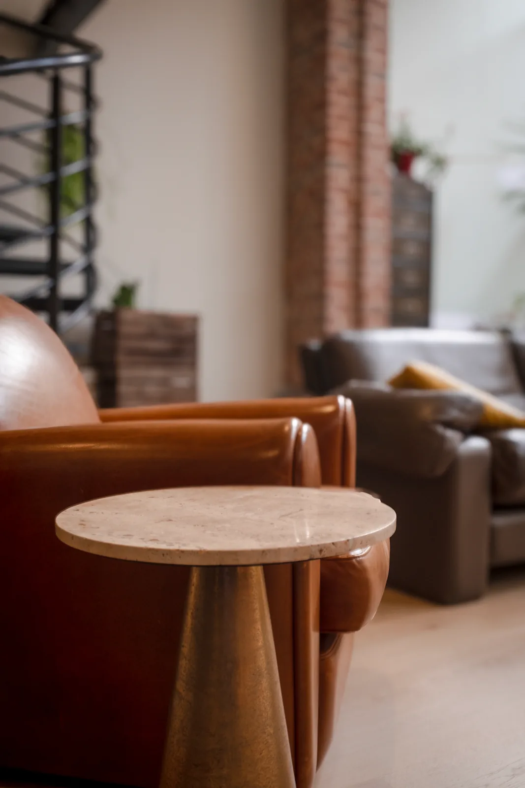Table d’appoint ronde devant les fauteuils bruns du salon.