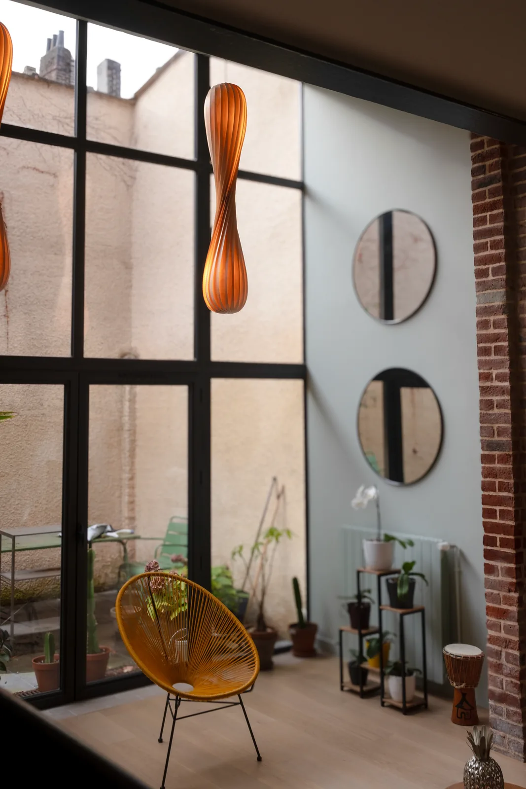 Coin repas près de la verrière avec fauteuil jaune et miroirs ronds.