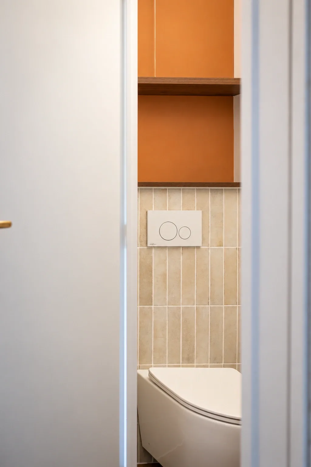 WC suspendu et étagères en bois dans une niche aux murs terracotta et au soubassement carrelé beige.