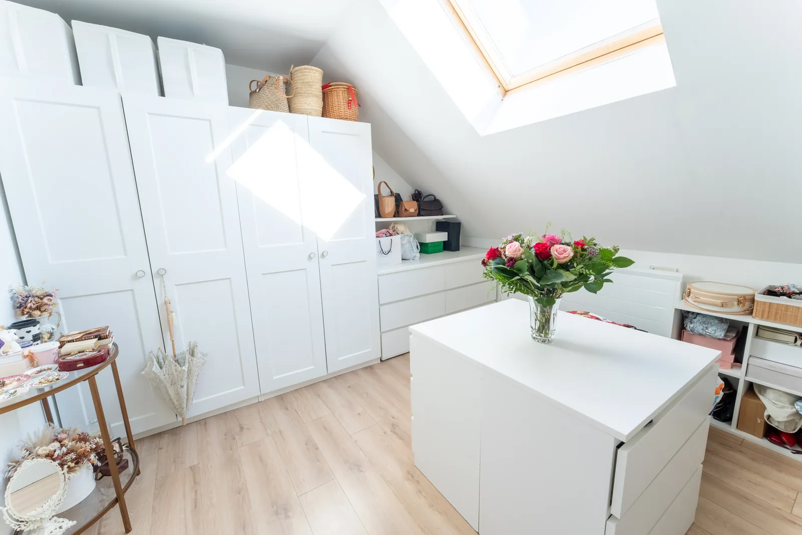 Dressing blanc sur mesure sous les combles avec îlot central et fenêtre de toit.