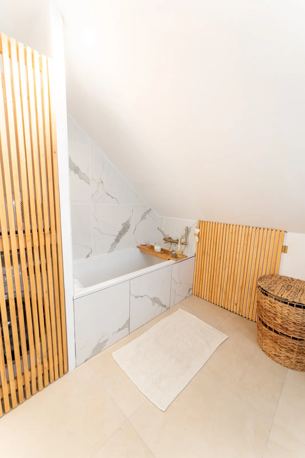 Baignoire sous pente habillée de marbre blanc et claustra en tasseaux de bois.