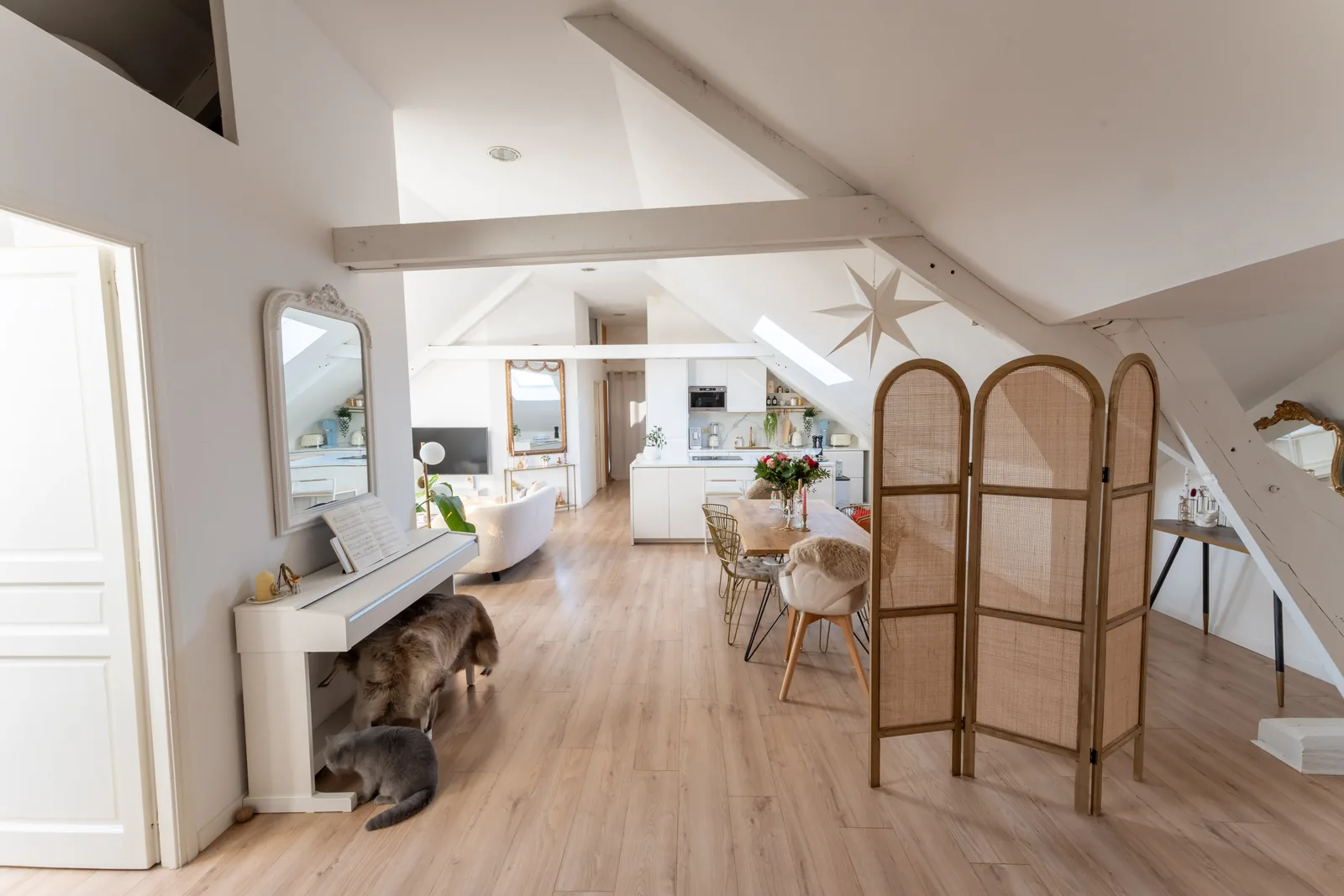 Pièce de vie du loft avec paravent en cannage, piano blanc et poutres apparentes peintes.