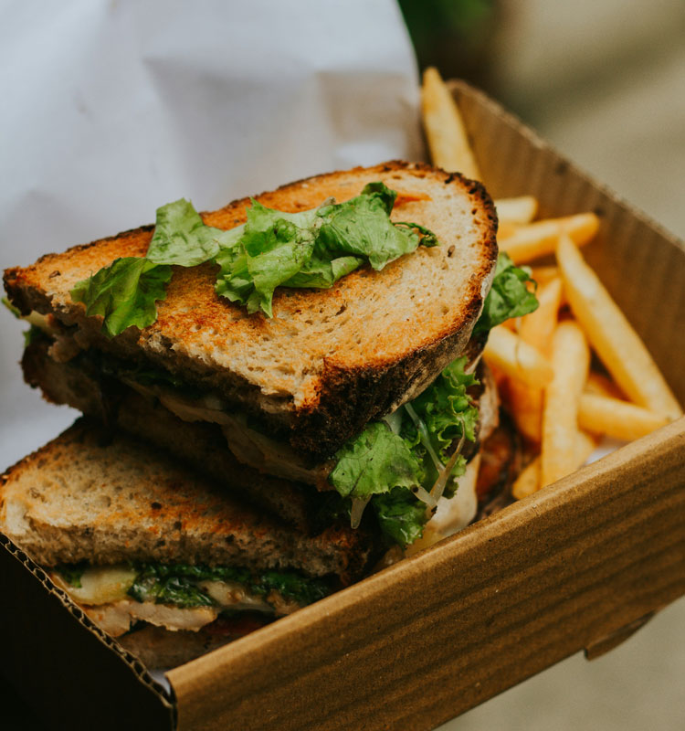 Sandwich toasté garni de salade verte, accompagné de frites, servi dans une boîte en carton pour une formule snacking à emporter.